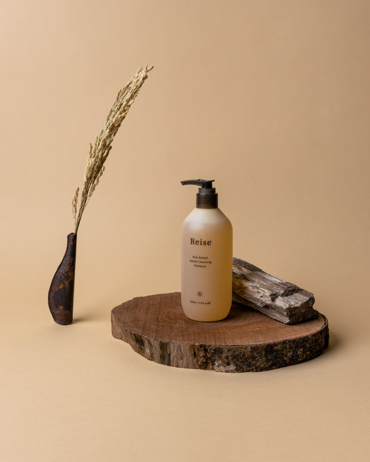 White bottle labeled 'Reise' on a wooden platform with a vase and stone on a beige background