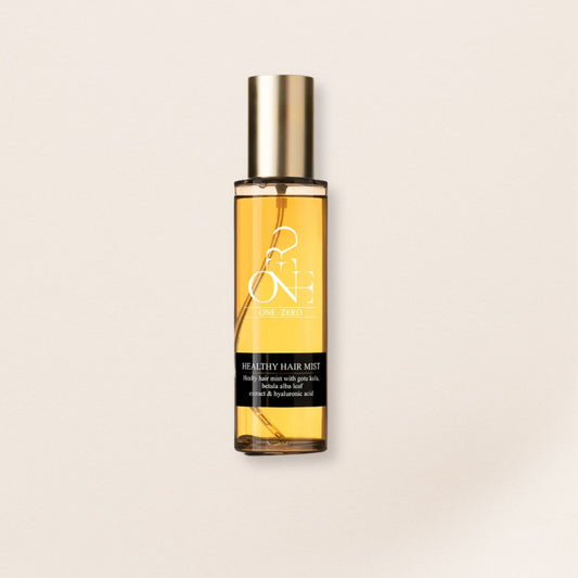 Hair mist bottle with gold cap and yellow liquid for fine hair on a beige background