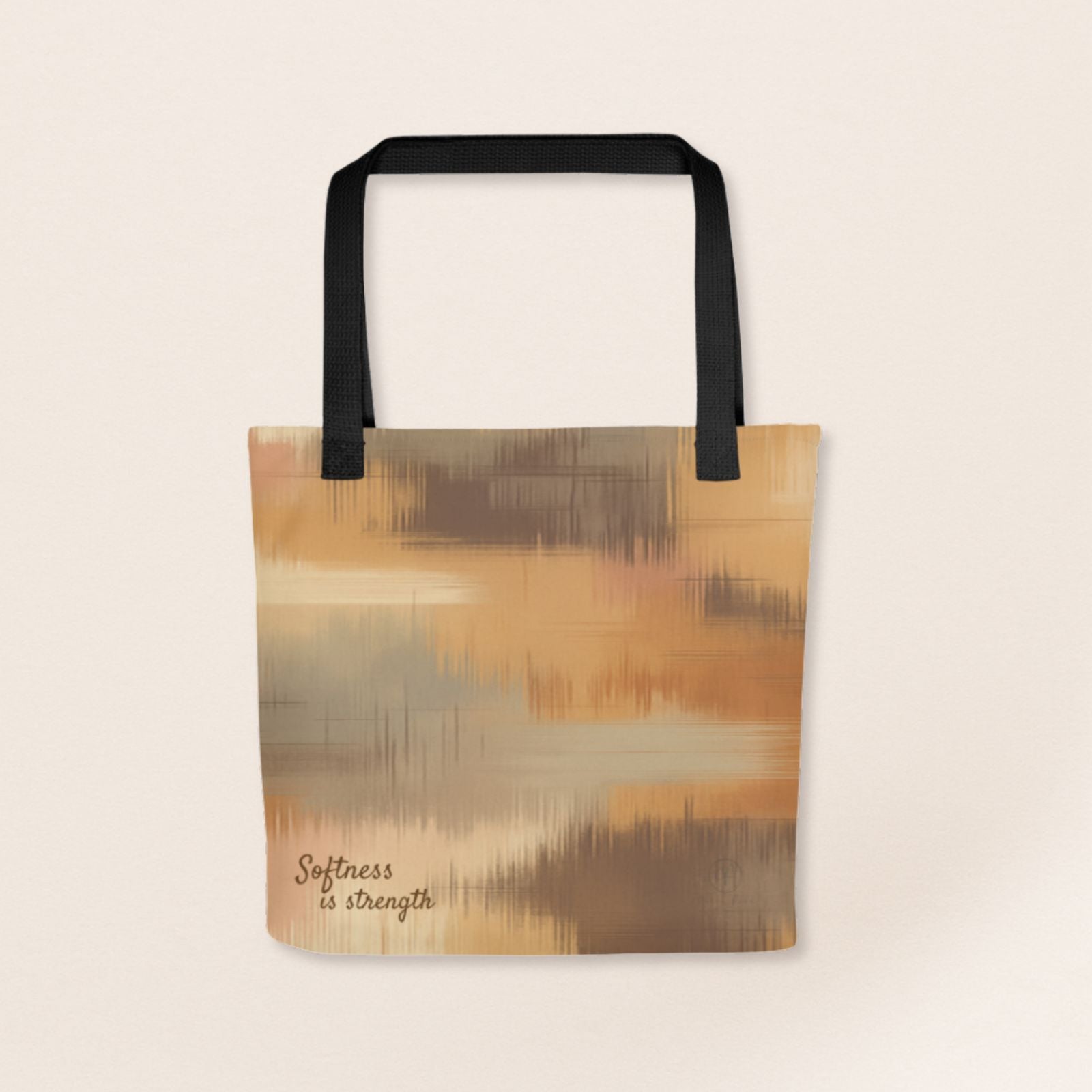 Beige and brown patterned tote bag with black handles and the phrase “Softness is strength” printed on the bottom right.