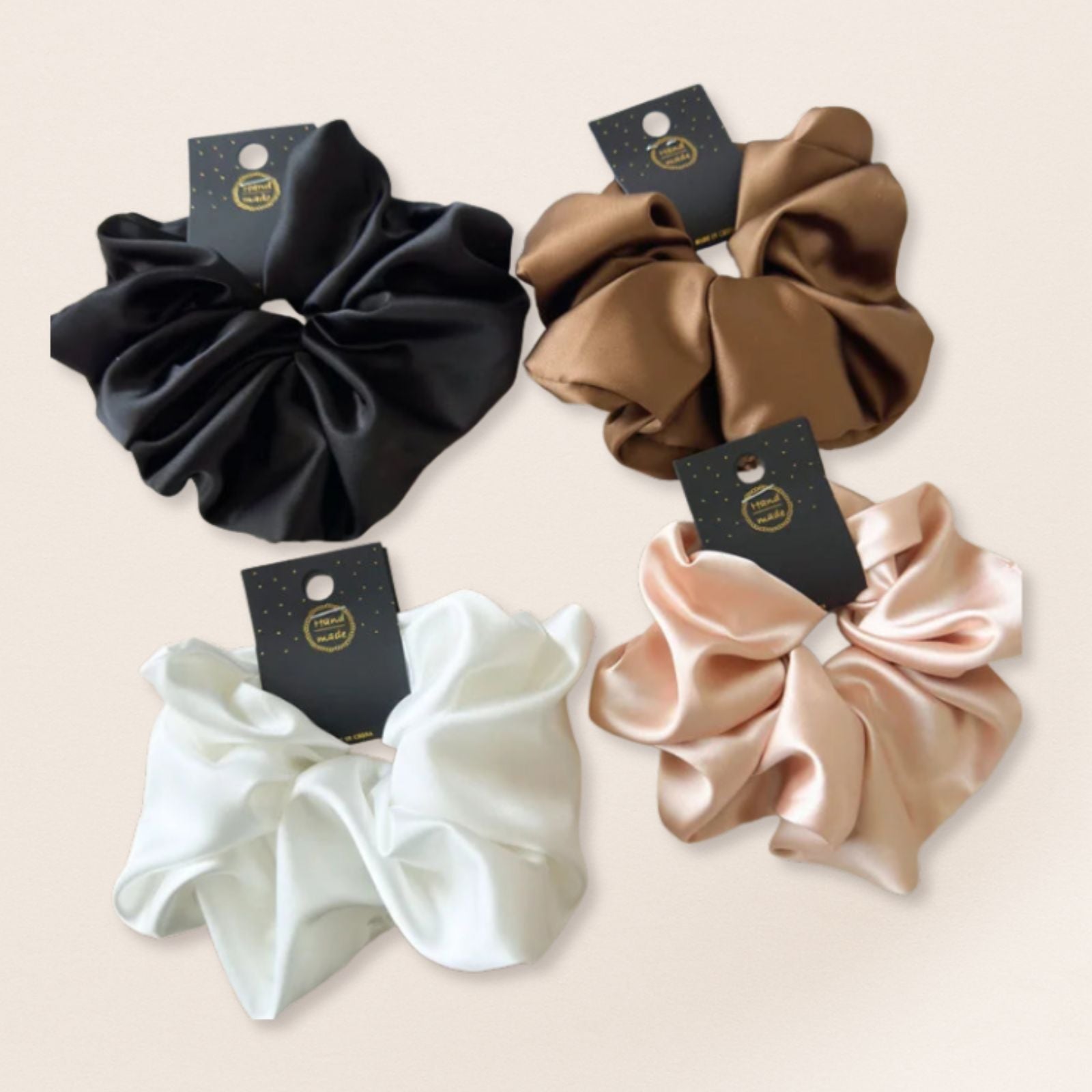 Four satin scrunchies in black, brown, white, and beige on a light beige background.