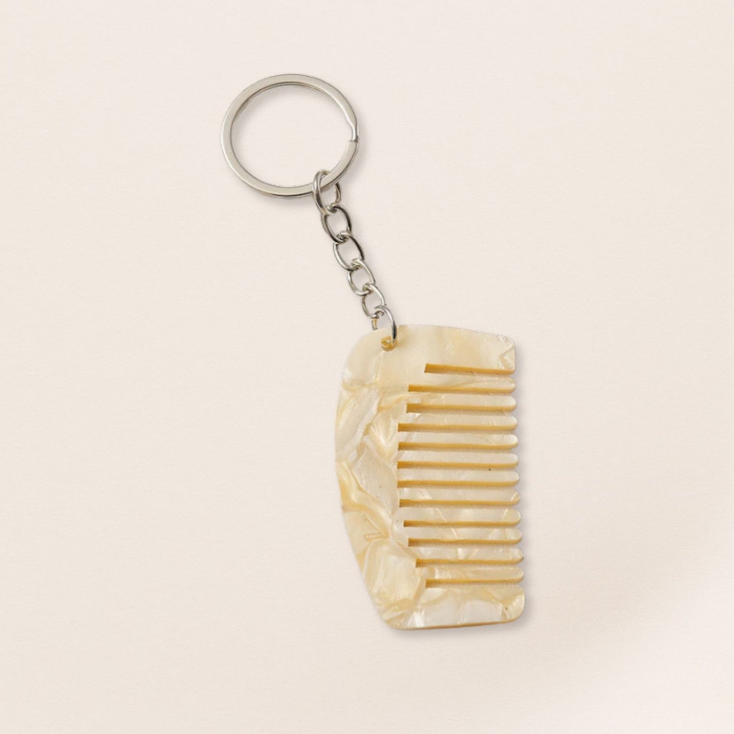 Mini white marbled comb keyring with silver chain on a beige background.