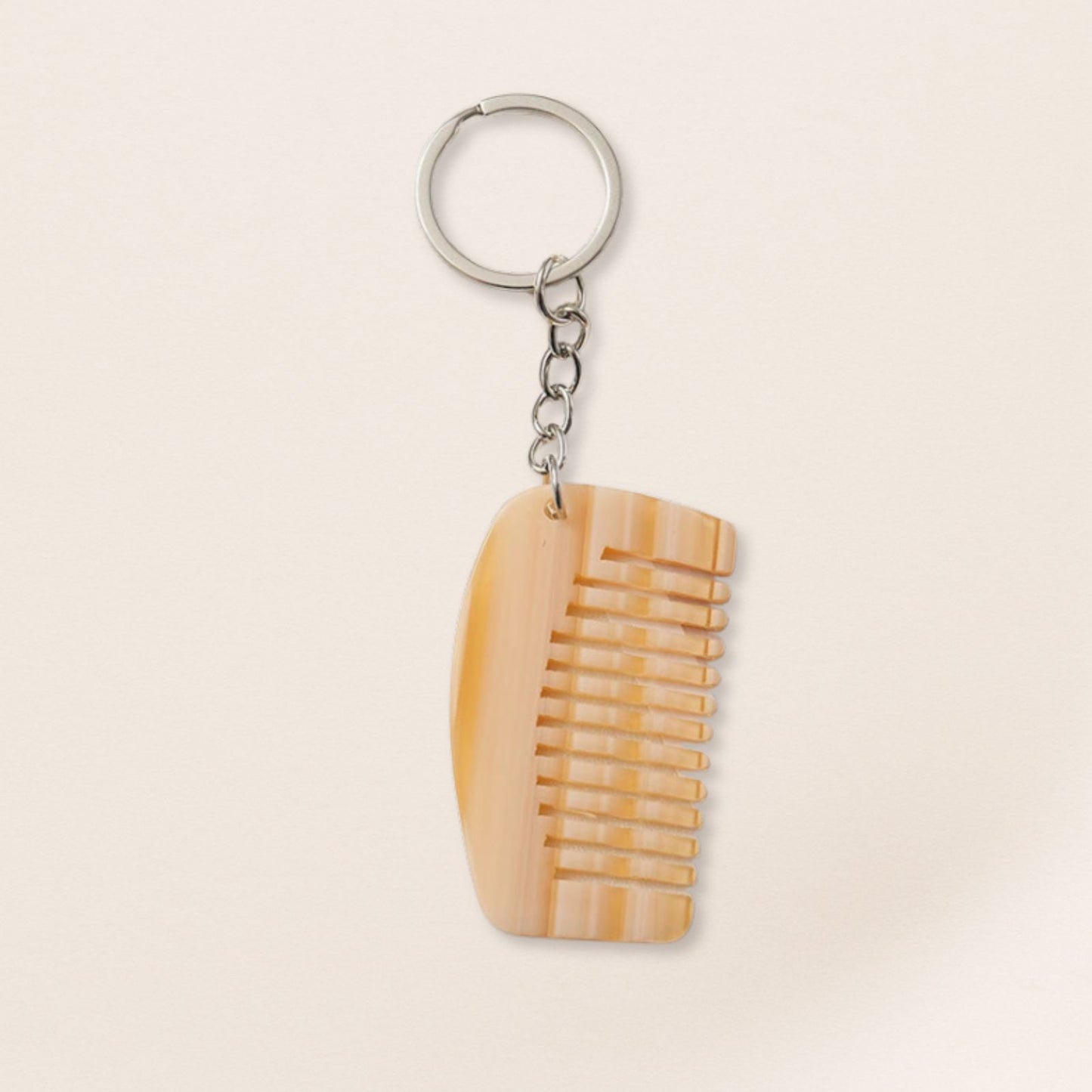 Mini cream marbled comb keyring with silver chain on a beige background.